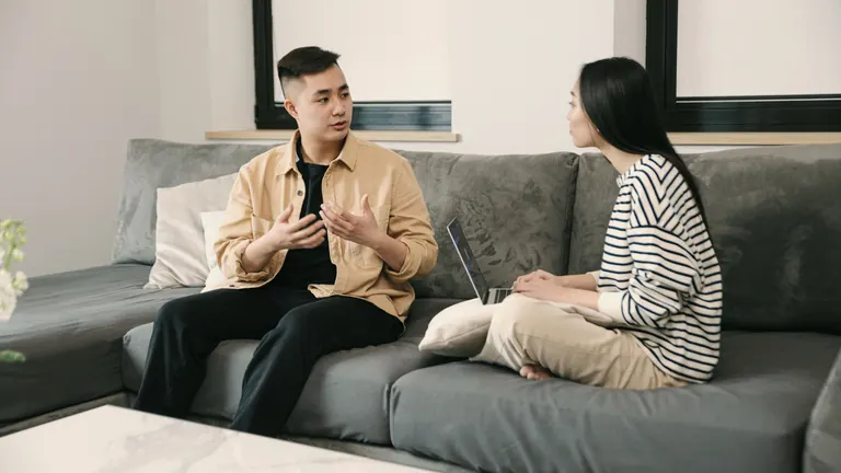 Two people talking on a grey sofa in a bright living room