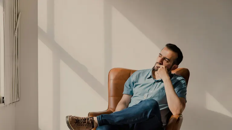 A man sitting in a leather armchair by a sunlit window, deep in thought