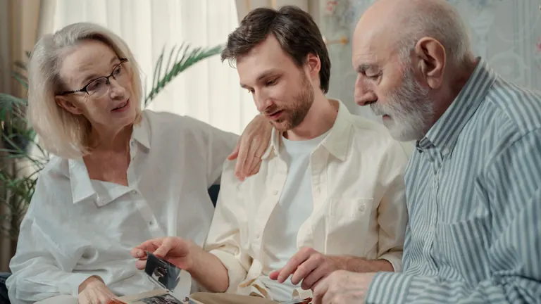 Parents and their adult son looking through a photo album together