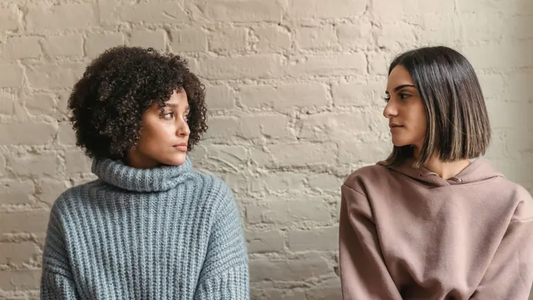 Two women sitting side by side against a white brick wall, in a quiet, serious conversation