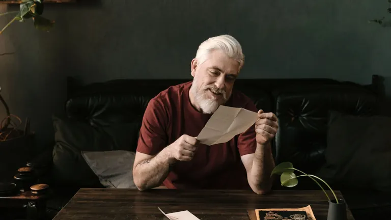 A man at home reading a printed letter, with a small smile