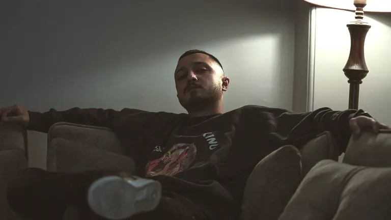 A man resting on a sofa at night under a lamp, awake