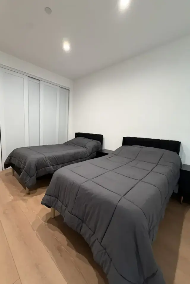 Bright bedroom with two made beds in grey linens and a mirrored closet