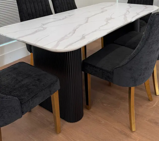Marble dining table on a fluted black base, with charcoal velvet chairs on brass legs