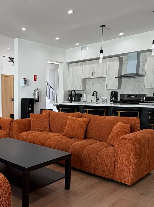Great room with a curved terracotta sofa, a black coffee table and the open kitchen behind