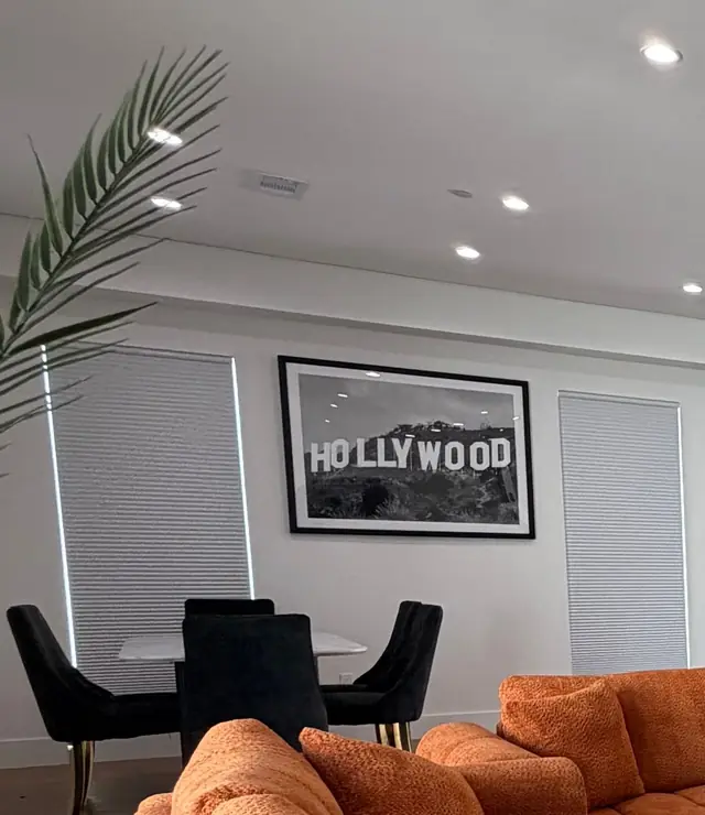 Dining table with black velvet chairs beneath a framed Hollywood sign print, palm fronds in the foreground