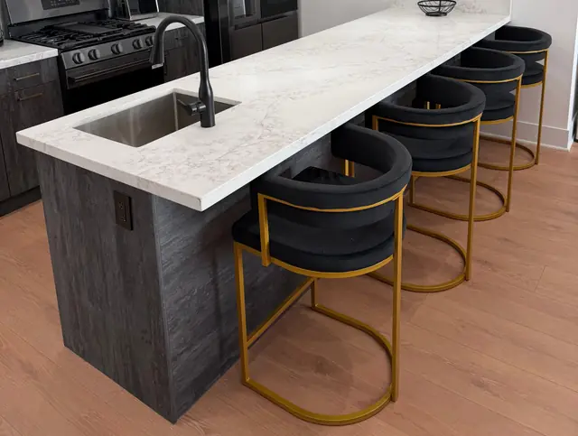 Kitchen island with a white stone counter and black velvet stools on gold frames