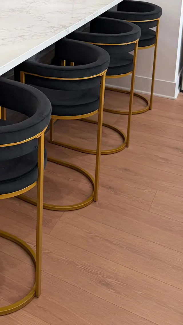 Gold-framed black velvet bar stools lined up along a white stone kitchen counter