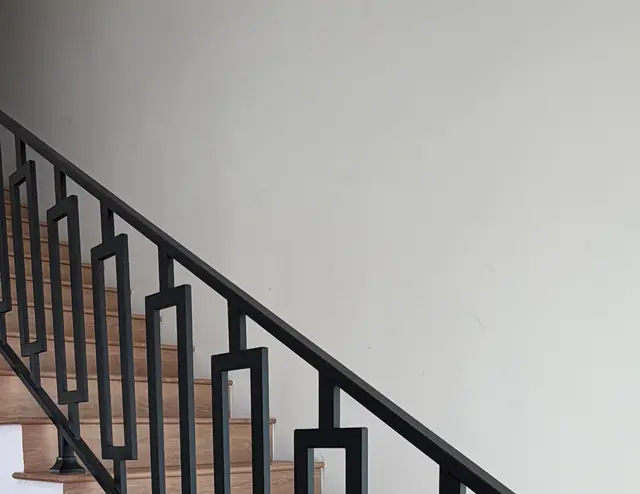 Oak staircase with a black geometric iron railing against a pale wall